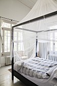 Black four-poster bed with mosquito net in white bedroom