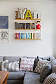 Grey couch with various scatter cushions below books and decorative letters on String shelves