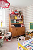 Various small cases, toys and soft toys on retro dresser in girl's bedroom