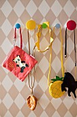 Various children's bags hung from colourful pegs on diamond-patterned wallpaper