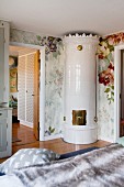 Elegant hand-crafted tiled stove in corner of bedroom with floral wallpaper