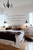 Animal-skin rug and scatter cushions on double bed below motto on wall of bedroom