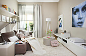 Sofa, standard lamp and low sideboard in cosy, beige living room with large artworks on wall