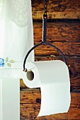 Toilet roll hung from old iron holder against rustic wooden wall