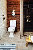 Toilette vor rustikaler Holzwand neben offener Dusche