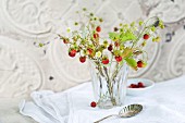 Glas mit einem Strauss wilder Erdbeeren mit Blüten