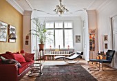Red sofa, side table, designer chaise and potted palm in window bay of lounge