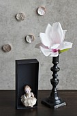 Magnolia flower in black candlestick, china figurine in black box and mother-of-pearl ornaments on wall