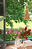 Blumenstrauss in weisser Krugvase neben Bücherstapel auf Fenstersims in offenem Fenster