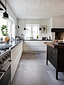 White L-shaped kitchen counter, black pendant lamps and island counter made from old workbench