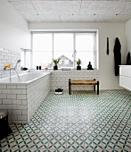 Bathtub below large window in bathroom with green and white patterned floor tiles