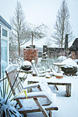 Garden in winter with snow cover and wooden furniture