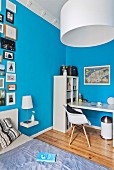 White desk and open-fronted shelves in bedroom with gallery of pictures of bright blue walls
