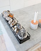 Pebbles painted with fish motifs in glass tray next to candlestick on concrete surface