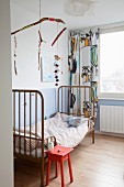 Mobile made from branches above metal bed in child's bedroom
