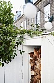 Stacked firewood in white wood-clad niche topped by climbing plant in front of traditional brick terrace façade