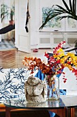 Ethnic sculpture and glass vase holding twigs of colourful leaves on coffee table