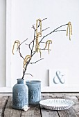 Branches of hazel catkins in vase with structured surface and matching beaker