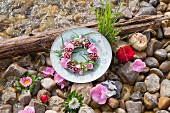 Wreath of flowers on plate and flowers on pebbles next to water
