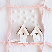 Small house ornaments surrounded by frame made from pink wool on white surfae