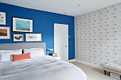 Gallery of pictures on blue wall and wallpaper with graphic patter in bedroom