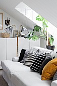 Various scatter cushions on comfortable sofa, retro standard lamp and house plant under sloping attic ceiling