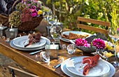 Gedeckter Tisch im herbstlichen Garten, dekoriert mit Rotkohl, Hortensienblüten, Astern und Dahlien
