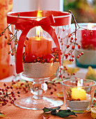 Rosa (Hagebutten), Malus (Zierapfel), Glaspokal mit Sand, orange Kerze