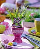 Easter grass seeded in pink egg cups, wood flowers, sugar eggs, napkin