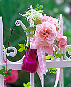 Blüte von Rosa (Rose), Clematis (Waldrebe) in pinkem Glasfläschchen