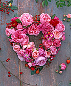 Kranz in Herzform aus Rosa (Rosen, rosa und Hagebutten) auf Holz