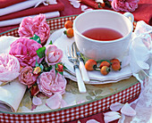 Bunch of pink rosa (rose, rosehips) on rolled napkin, teacup