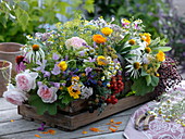 Wooden basket with arrangement of fresh cut flowers, herbs and berries