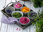 Schälchen mit Blüten und Blättern von Tee- und Duftkräutern