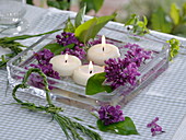 Syringa flowers and leaves with floating candles in glass bowl