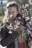 Woman sniffing at blossoming Viburnum bodnantense 'Dawn' branch
