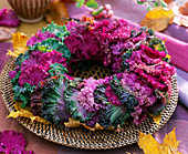 Brassica wreath with ornamental cabbage leaves on plaited coaster, autumn leaves