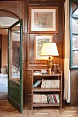 Table lamp on bookshelves against wood-panelled wall in hallway