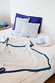 Blanket with blue crocheted trim and breakfast crockery on bed