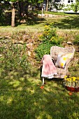 Blanket and printed cushion on wicker armchair on lawn