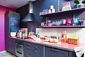 Dark kitchen counter with pink worksurface below hot pink shelves