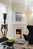 Glas-Couchtisch und Designer-Sessel vor Kamin und Säulenvasi in elegantem Wohnzimmer