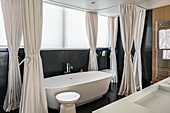 Free-standing bathtub with curtains in designer bathroom