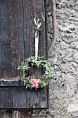 Wreath of ivy with pink flowers hung from rustic shutter