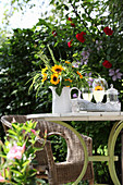 Sunflowers and ornamental grasses in jug on garden table with wicker armchair in background