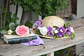 Straw hat with wreath of flowers next to rose on book in garden