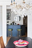 Crystal chandelier above dining table in front of kitchen counter and retro bar stools