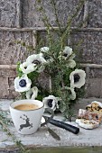 Cup with stag motif and sliced stollen in front of wreath of anemones
