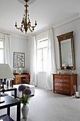 Antique chest of drawers below gilt-framed mirror on wall in lounge