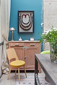 Large framed necklace above old cabinet on blue wall